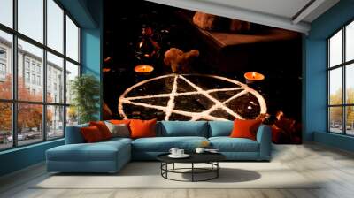 Pentagram made of salt, a pagan symbol used for protection by the wiccan community,  surrounded by candles, herbs and spices on a black shiny table top. Wall mural