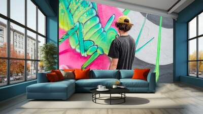 A young graffiti artist drawing street art in green and pink tones. Wall mural