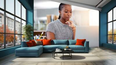 Laptop, research and a business black woman thinking while working at her desk in her office with flare. Computer, planning and idea with a serious young female employee reading an email at work Wall mural