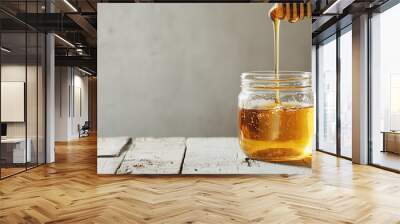 jar of honey with a honey dipper dripping golden honey into it on a wooden table Wall mural