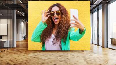 Selfie, fashion and woman with sunglasses on yellow background, color wall and gen z backdrop. Happy young female, trendy style and take profile picture on social media, green clothes and curly hair Wall mural