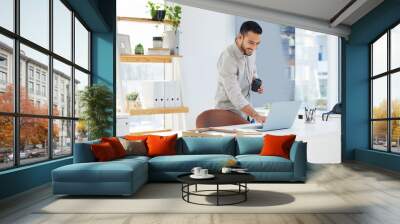 Feeling positive today. Shot of a young man using his laptop at work in a modern office. Wall mural