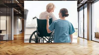 Old woman in wheelchair, care or caregiver talking for healthcare support at nursing home. Back, view or happy nurse speaking to senior patient or elderly person with a disability for empathy or hope Wall mural