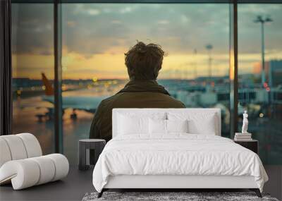 a man is standing in front of a window at an airport, looking out at the planes Wall mural