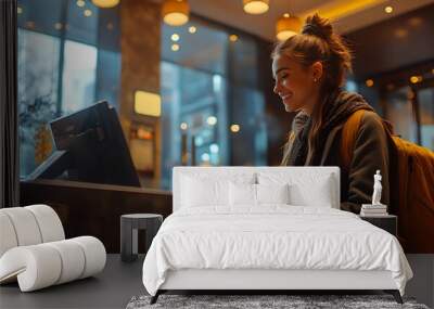 A woman is sitting at a desk in a hotel lobby, smiling and typing on a computer Wall mural