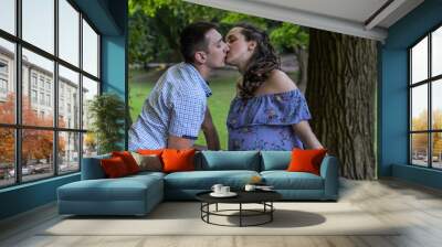 Young couple in love husband and pregnant wife kiss in the park, happy family Wall mural