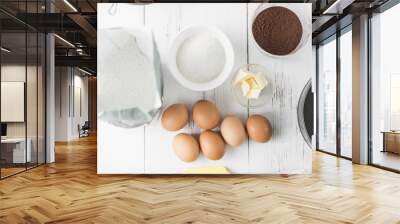 Ingredients for cooking: eggs, flour, sugar, cocoa powder, butter on a white wooden background, top view Wall mural