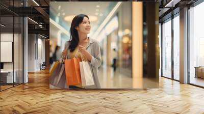 Cheerful Asian woman holding shopping bags. Beautiful young Asian woman shopping in the mall. Wall mural