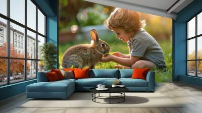 A young child sits in a grassy field, smiling as they gently pet a brown rabbit. Wall mural