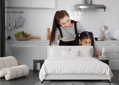 Smiling Asian mother and little asian girl child is learning online with laptop and cooking for baking bakery on wooden table together Homemade pastry for bread. Family love and Homeschool Concept. Wall mural