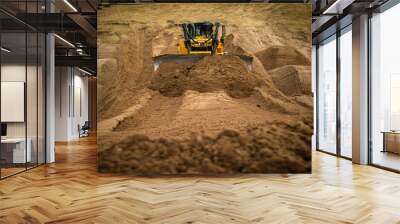 A yellow bulldozer pushes a full load of material into a pile. Wall mural