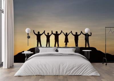 Silhouette of people are celebrating success at the top of the mountain, sky and sun light background. Team business concept. Wall mural