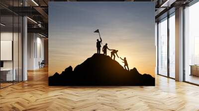 Silhouette of people helping each other hike up a mountain at sunset background. Teamwork, success and goal concept. Wall mural