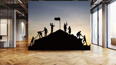 Silhouette of people helping each other hike up a mountain at sunset background. Teamwork, success and goal concept. Wall mural