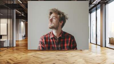 Portrait of a blissful caucasian man in his 20s dressed in a relaxed flannel shirt while standing against minimalist or empty room background Wall mural