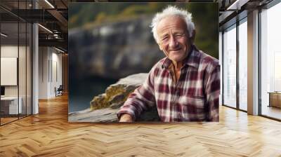 portrait of a grinning man in his 70s dressed in a relaxed flannel shirt against a rocky cliff backg Wall mural