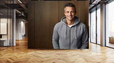 Portrait of a happy man in his 40s wearing a zip-up fleece hoodie against a light wood minimalistic setup. AI Generation Wall mural