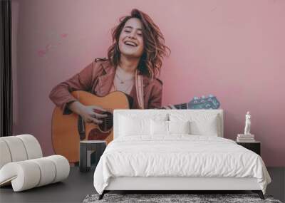 Portrait of a happy woman in her 30s playing the guitar while standing against solid pastel color wall Wall mural