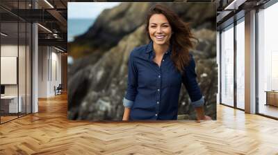 Portrait of a joyful woman in her 30s sporting a versatile denim shirt against a rocky shoreline background. AI Generation Wall mural