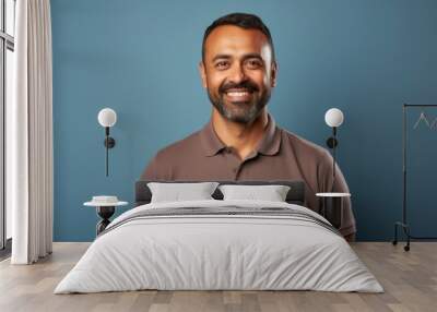 Portrait of a merry indian man in his 40s wearing a sporty polo shirt while standing against light wood minimalistic setup Wall mural