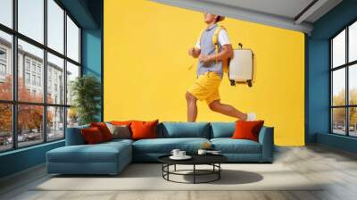 An energetic man in casual summer clothes runs holding a white suitcase on wheels in a yellow-themed scene, creating a dynamic atmosphere. Wall mural