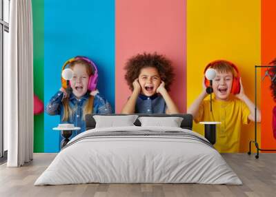 Five children of different ages stand joyfully together against the backdrop of a multi-coloured rainbow, each wearing different coloured headphones. Wall mural