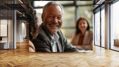 Image shows a group of four diverse business people in a meeting. The man in a gray sweater smiles, set in a professional and warm atmosphere with active discussions. Wall mural