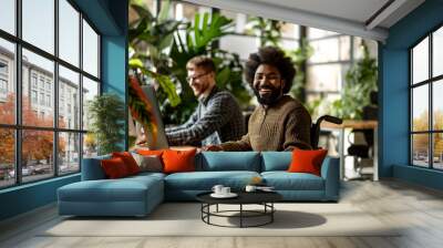 A young african american man with disability smiling and looking in the camera while working on laptop in modern office Wall mural