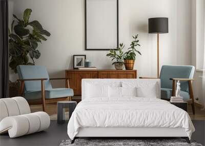 Mockup of a blank white poster frame on the wall in a mid century modern living room with blue chairs, wood sideboard and plants Wall mural