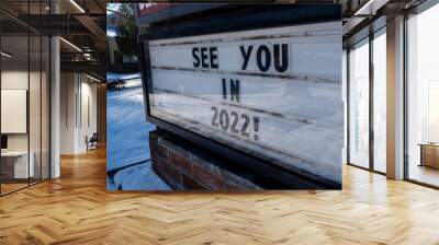 Angled view of a school changeable letter sign on a snowy day that says See You in 2022! Wall mural