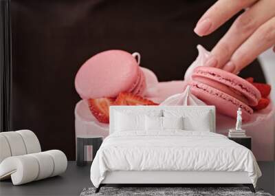 Woman pastry chef decorates pink cake with macaroons and berries, close-up. Cake making process, Selective focus. Banner format Wall mural