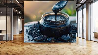 A detailed close-up shot of an open black jar of liquid Shilajit with a spoon, set on a rocky surface with sunlight and greenery in the background. Wall mural