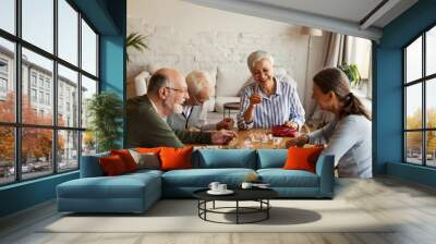 Group of four cheerful senior people, two men and two women, having fun sitting at table and playing bingo game in nursing home Wall mural