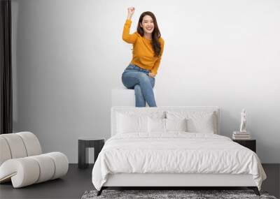 Attractive beautiful Asian woman sitting on white box and hands up raised arms from happiness, Excited female and winner success concept Wall mural