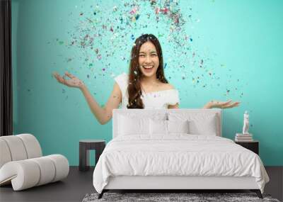 Cheerful young Asian woman celebrating with colorful confetti isolated on green background, Thai model Wall mural