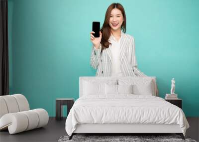 Happy asian woman smile and holding mobile phone isolated over light green background Wall mural