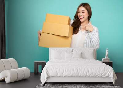 Happy Asian woman smiling and holding package parcel box isolated on light green background, Delivery courier and shipping service concept Wall mural