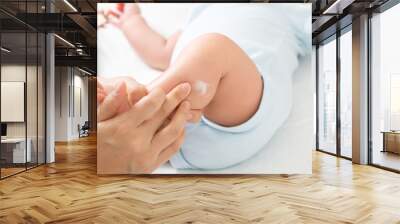 Mother is applying cream to the baby boy which helps to maintain skin leg hydration, Skincare and moisturizing cream concept Wall mural