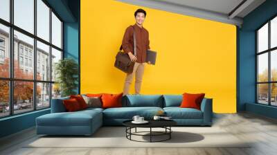 Portrait of young Asian businessman smile and holding laptop and brown leather bag isolated on yellow background, Full body composition Wall mural