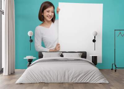 Smiling happy Asian woman holding and standing behind big white poster isolated on light green background Wall mural