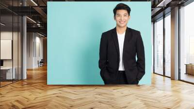 Smiling young Asian businessman in black suit isolated on green background Wall mural