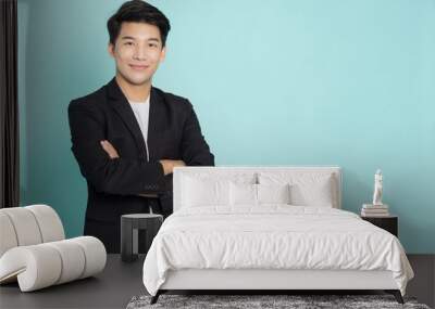 Smiling young Asian businessman with arms crossed isolated on green background Wall mural