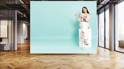 young asian businesswoman sitting and pointing to empty copy space isolated on green background Wall mural