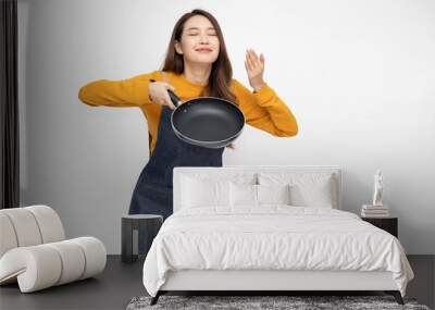 Young Asian woman housewife wearing kitchen apron cooking and holding pan isolated on white background Wall mural