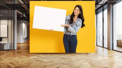 Young asian woman showing and holding blank white billboard isolated on yellow background Wall mural