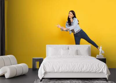 Young beautiful Asian woman standing and pointing to empty copy space isolated on yellow background, Full body composition Wall mural