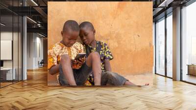 african kids using a smartphone. two african children viewing content on a mobile phone together Wall mural