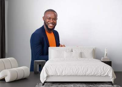 handsome young black man wearing a suit using his phone feeling excited and happy, sitting against a white plain background Wall mural