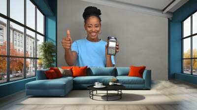 pretty black lady smiling while holding and showing a point of sale device, gives thumbs up Wall mural