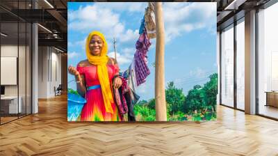 pretty young african woman hanging clothes on a line to dry outside after doing laundry Wall mural